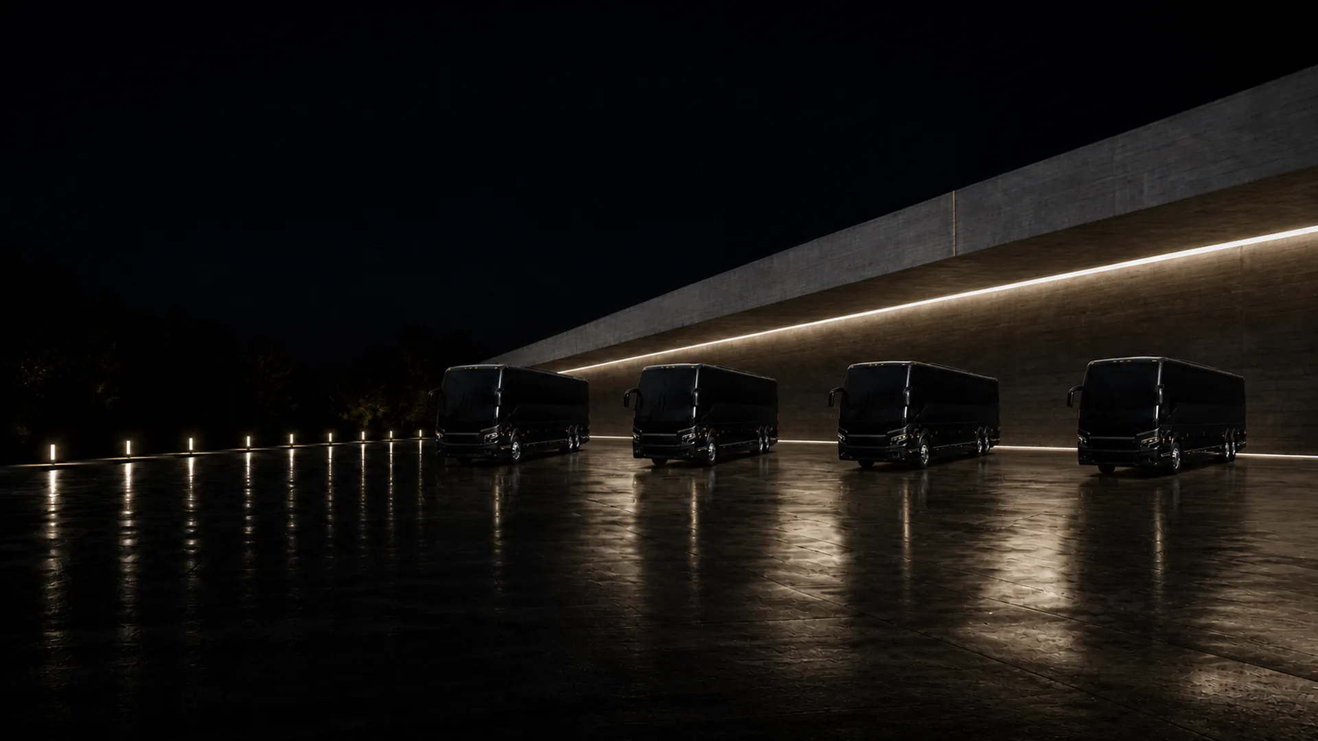 Four black Prevost H3-45 motorcoaches parked nose-out in a fanned arc on a wet lot at night, lit by a row of low ground lights.